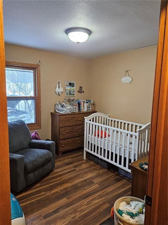 bedroom with a textured ceiling, a nursery area, and dark hardwood / wood-style floors