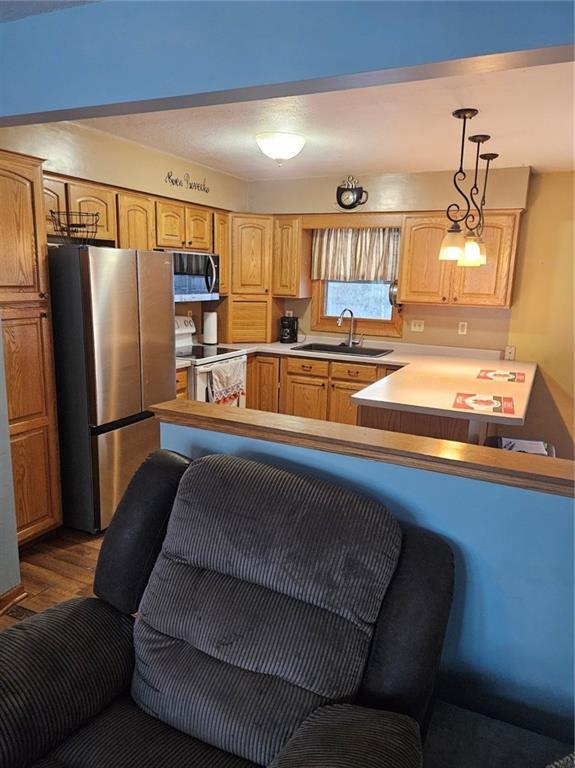 kitchen featuring stainless steel appliances, sink, hanging light fixtures, kitchen peninsula, and hardwood / wood-style flooring