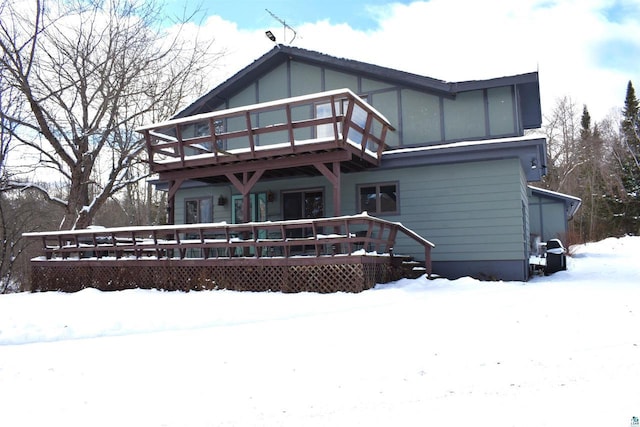 snow covered rear of property featuring a balcony and a wooden deck