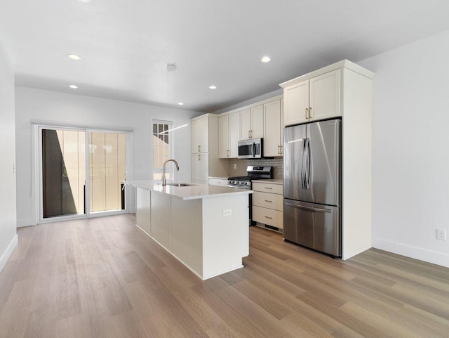 kitchen with white cabinets, appliances with stainless steel finishes, light hardwood / wood-style floors, sink, and a kitchen island with sink