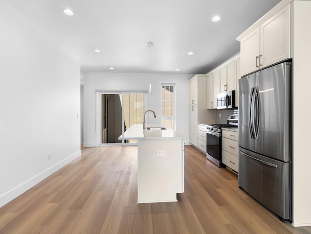 kitchen featuring white cabinetry, stainless steel appliances, decorative backsplash, sink, and a center island with sink