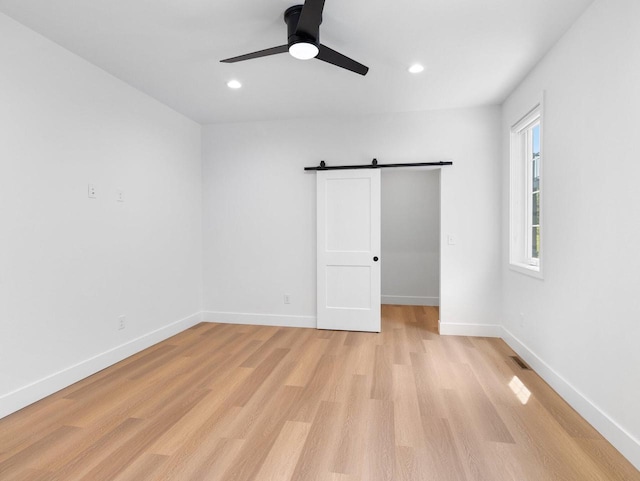 empty room with ceiling fan, a barn door, and light hardwood / wood-style floors