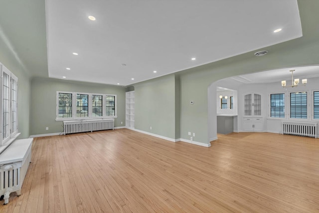 unfurnished living room featuring light hardwood / wood-style floors, radiator, and a notable chandelier