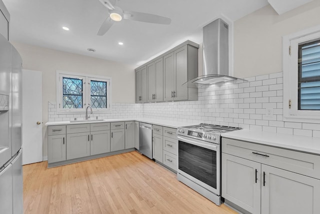 kitchen with ceiling fan, backsplash, sink, stainless steel appliances, and wall chimney exhaust hood