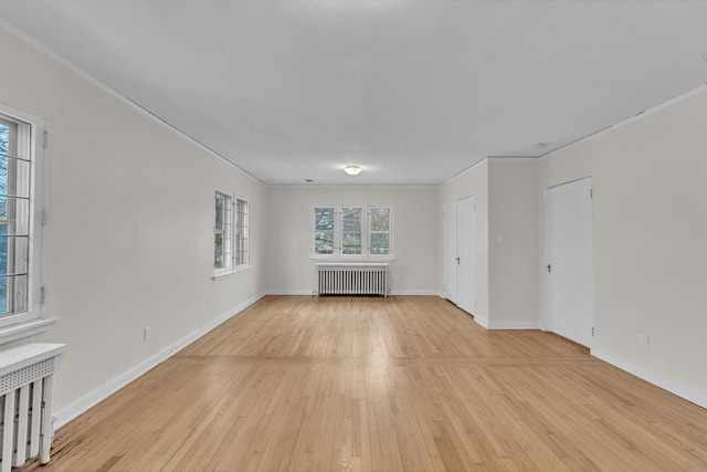 unfurnished living room featuring radiator, light wood-type flooring, and ornamental molding