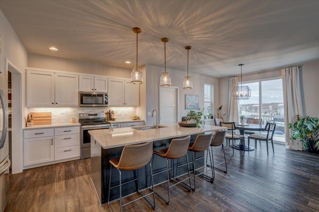 kitchen with white cabinets, appliances with stainless steel finishes, decorative light fixtures, sink, and a kitchen island with sink