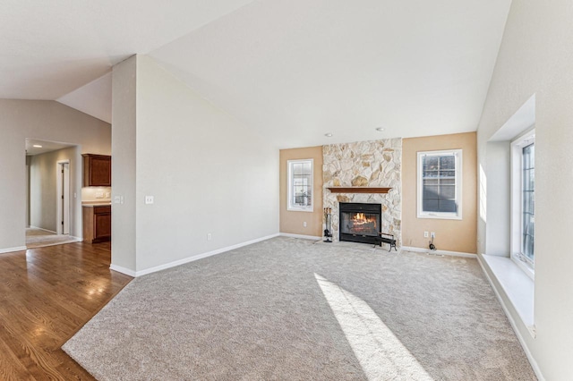 unfurnished living room with vaulted ceiling, hardwood / wood-style flooring, and a stone fireplace