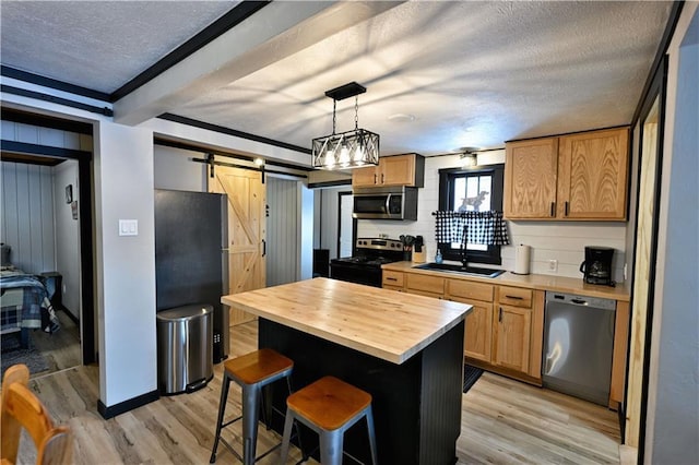 kitchen featuring a barn door, a kitchen island, sink, appliances with stainless steel finishes, and wood counters