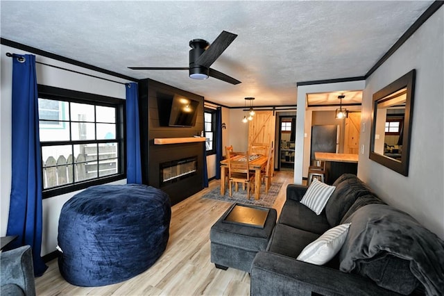 living room featuring a barn door, a large fireplace, crown molding, light wood-type flooring, and a textured ceiling