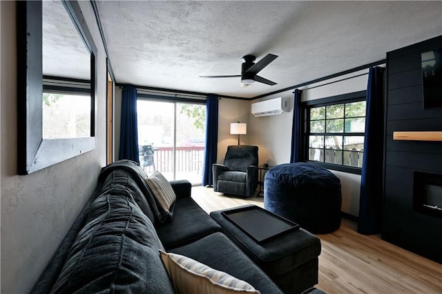 living room with a textured ceiling, ceiling fan, light hardwood / wood-style flooring, and a wall mounted air conditioner