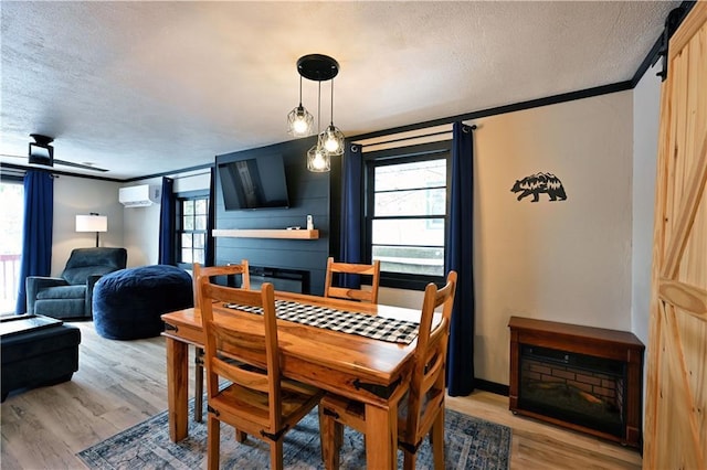 dining space featuring a wall mounted AC, a fireplace, a textured ceiling, and light hardwood / wood-style flooring