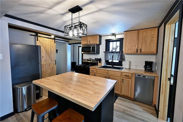 kitchen featuring stainless steel appliances, tasteful backsplash, sink, hanging light fixtures, and a barn door