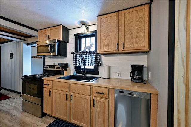 kitchen with light hardwood / wood-style floors, appliances with stainless steel finishes, a textured ceiling, ornamental molding, and sink