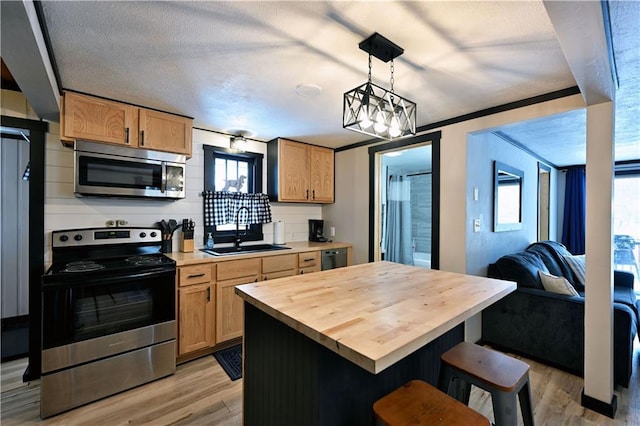 kitchen featuring appliances with stainless steel finishes, a center island, decorative light fixtures, sink, and ornamental molding