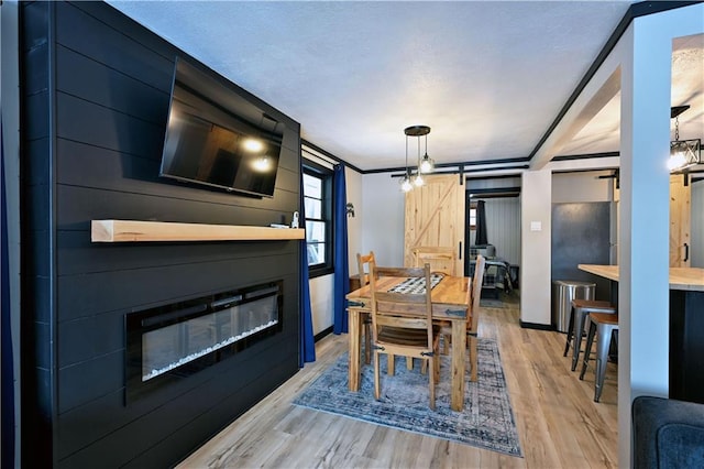 dining space with light hardwood / wood-style flooring, ornamental molding, a barn door, and a fireplace