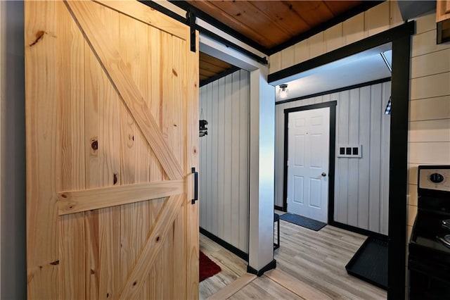 hallway with wood ceiling, a barn door, wood walls, and light hardwood / wood-style floors