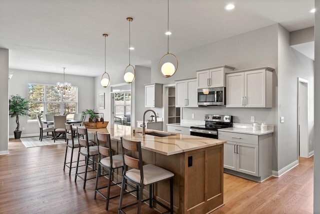 kitchen with appliances with stainless steel finishes, an island with sink, sink, hanging light fixtures, and light stone counters