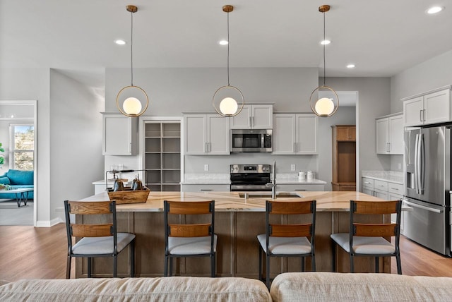 kitchen with white cabinets, pendant lighting, appliances with stainless steel finishes, and a kitchen island with sink