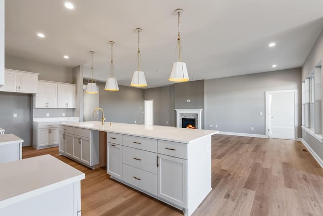 kitchen with white cabinetry, sink, pendant lighting, and a center island with sink