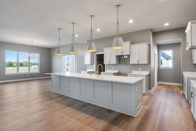 kitchen with decorative light fixtures, a large island with sink, light hardwood / wood-style floors, an inviting chandelier, and white cabinets