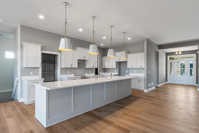 kitchen with hanging light fixtures, light wood-type flooring, a large island with sink, and white cabinetry