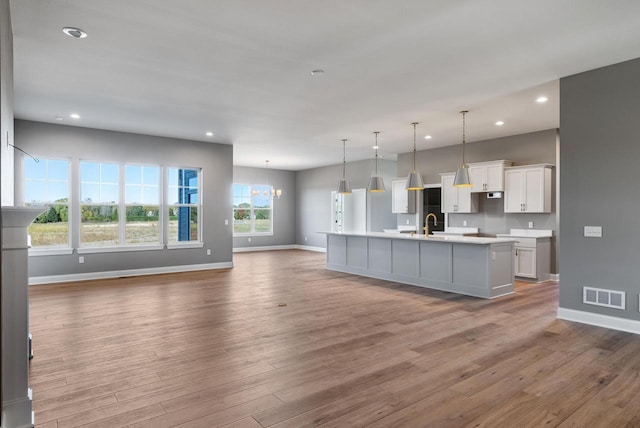 kitchen with an inviting chandelier, hardwood / wood-style flooring, an island with sink, hanging light fixtures, and white cabinets