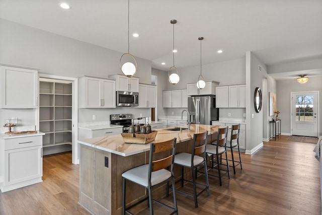 kitchen with appliances with stainless steel finishes, a kitchen island with sink, hanging light fixtures, white cabinets, and sink