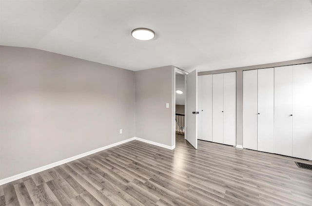 unfurnished bedroom with light hardwood / wood-style floors, two closets, and lofted ceiling