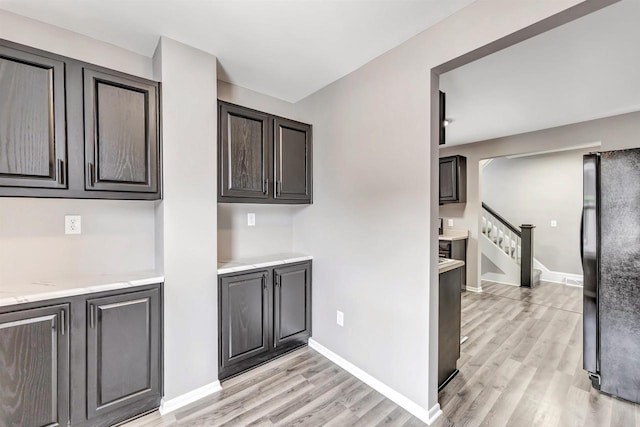 kitchen featuring dark brown cabinets, light hardwood / wood-style floors, and black refrigerator