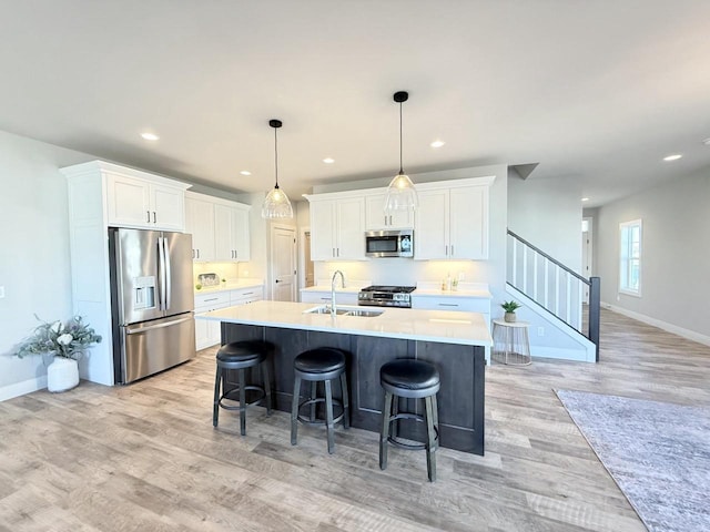 kitchen featuring white cabinets, appliances with stainless steel finishes, an island with sink, sink, and hanging light fixtures