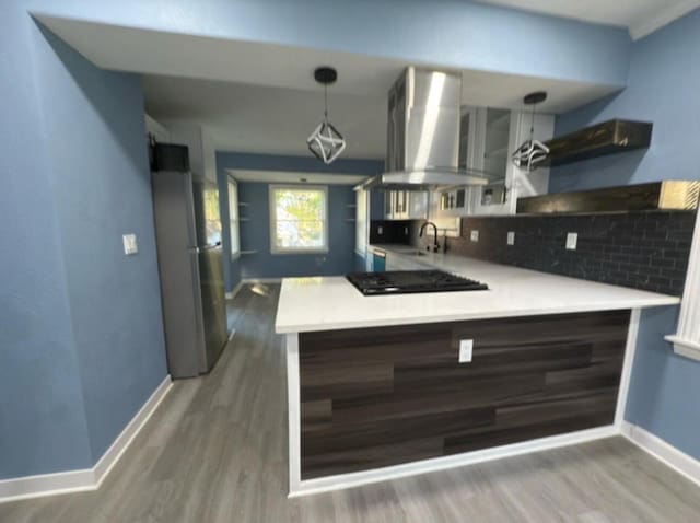 kitchen with wall chimney exhaust hood, tasteful backsplash, black gas cooktop, kitchen peninsula, and stainless steel refrigerator