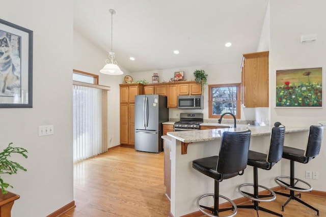 kitchen with kitchen peninsula, appliances with stainless steel finishes, a kitchen breakfast bar, light stone countertops, and light hardwood / wood-style flooring