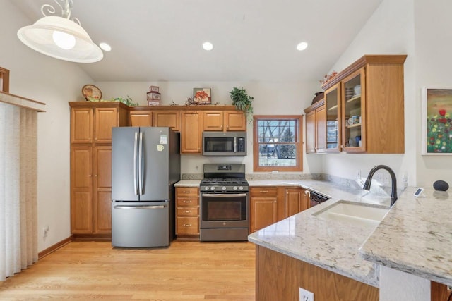 kitchen with pendant lighting, stainless steel appliances, sink, light wood-type flooring, and light stone counters