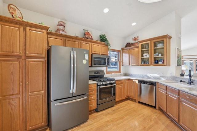 kitchen featuring lofted ceiling, sink, light wood-type flooring, stainless steel appliances, and light stone counters