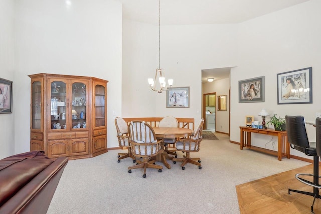 dining room with high vaulted ceiling, light colored carpet, washer / dryer, and an inviting chandelier