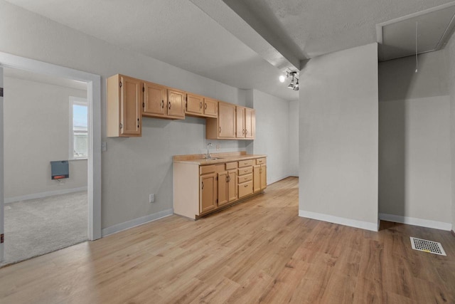 kitchen with light wood-type flooring, light brown cabinetry, a textured ceiling, and sink