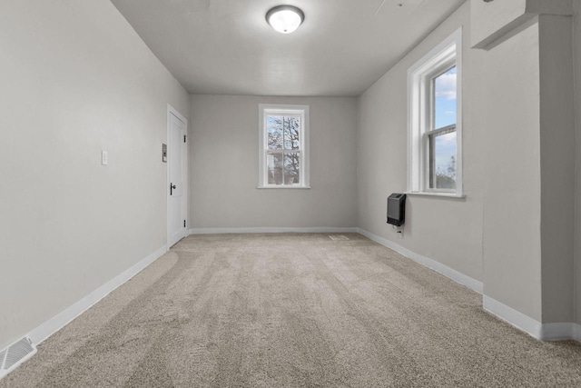 empty room with heating unit, light carpet, and a healthy amount of sunlight