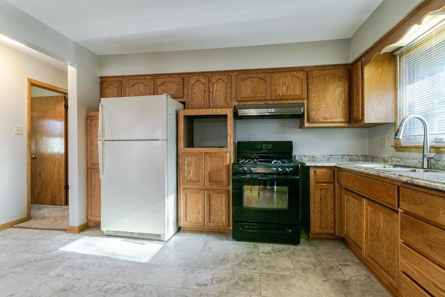 kitchen featuring white refrigerator, black gas range oven, light stone counters, and sink