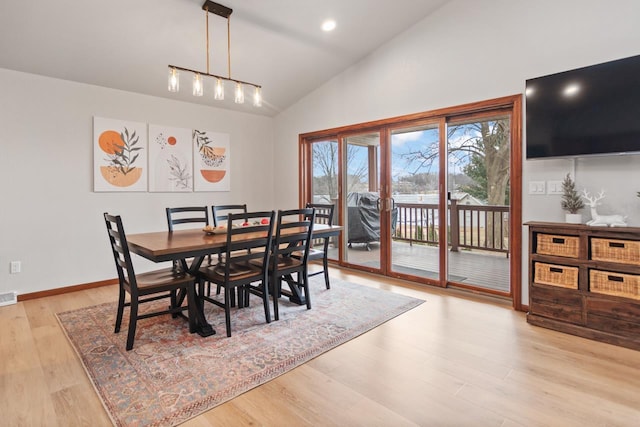 dining space with high vaulted ceiling, light wood-type flooring, and a notable chandelier