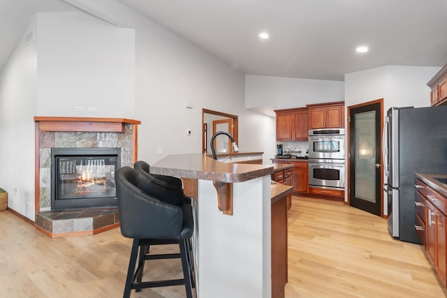 kitchen with appliances with stainless steel finishes, a kitchen bar, sink, light wood-type flooring, and a tile fireplace