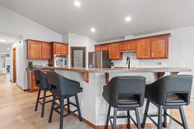 kitchen with light wood-type flooring, vaulted ceiling, a kitchen breakfast bar, and stainless steel appliances