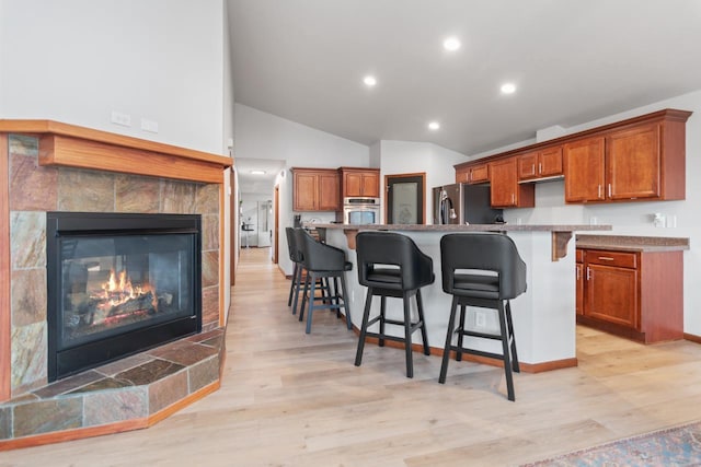 kitchen with stainless steel appliances, a kitchen island with sink, a breakfast bar, light hardwood / wood-style flooring, and a tiled fireplace