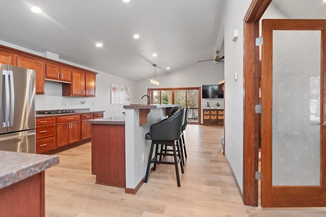 kitchen featuring lofted ceiling, black gas cooktop, stainless steel refrigerator, a center island with sink, and a breakfast bar area