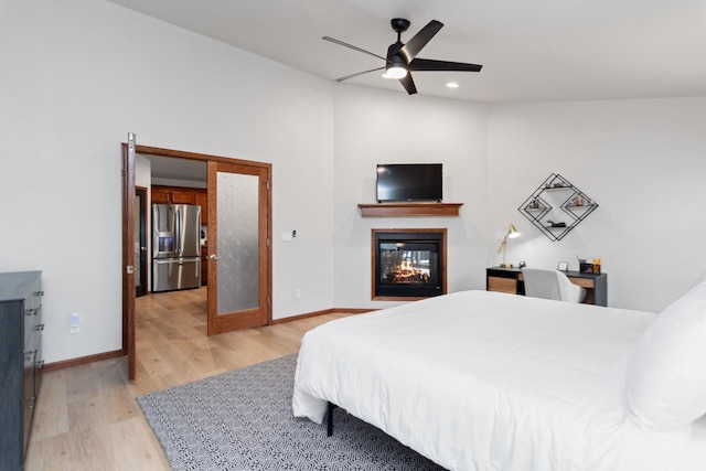 bedroom with ceiling fan, a multi sided fireplace, stainless steel fridge with ice dispenser, and light wood-type flooring