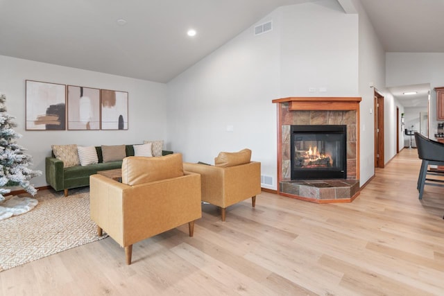 living room featuring light wood-type flooring, vaulted ceiling, and a tile fireplace