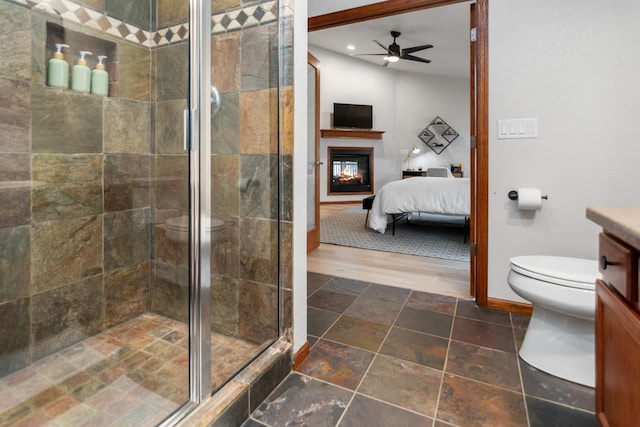 bathroom with vanity, a multi sided fireplace, ceiling fan, toilet, and a shower with shower door