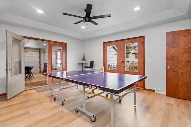 recreation room featuring a raised ceiling, french doors, light hardwood / wood-style floors, and ceiling fan