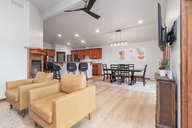 living room with ceiling fan, vaulted ceiling with beams, light wood-type flooring, and a fireplace