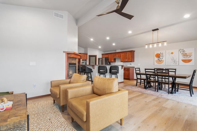 living room with vaulted ceiling, ceiling fan, a tiled fireplace, and light hardwood / wood-style flooring