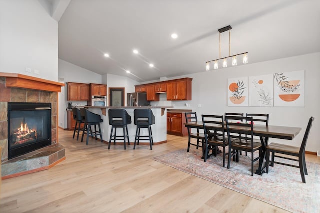 dining area featuring light wood-type flooring, vaulted ceiling, and a fireplace